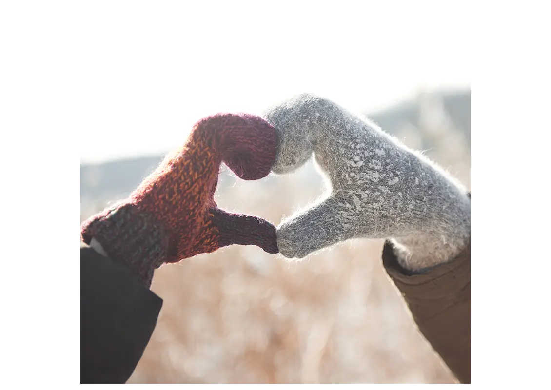 Two people wearing winter gloves making a heart shape with their hands